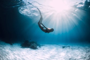 Kadın dalgıcı kumlu deniz üzerinde yüzgeçler ile yüzmek.