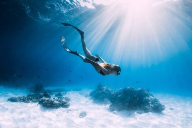 Kadın serbest dalgıç yüzgeçlerle kayar. kumlu deniz üzerinde. Mavi okyanusta serbest dalış ve güzel ışık