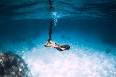 Mavi okyanusta serbest dalış. Kadın serbest dalgıç yüzgeçli kumlu deniz üzerinde kayar.