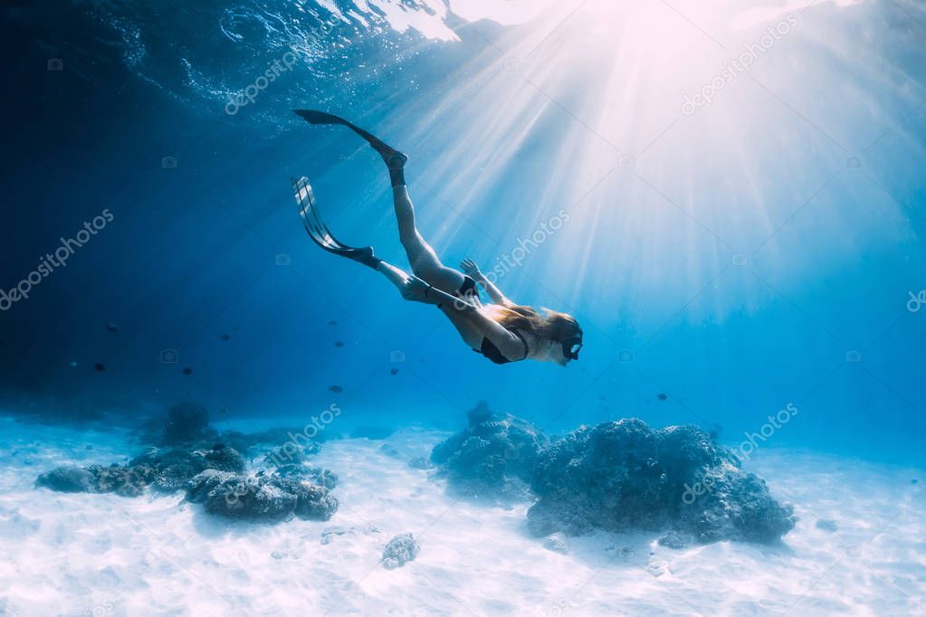 Woman freediver glides with fins. over sandy sea. Freediving and beautiful light in blue ocean