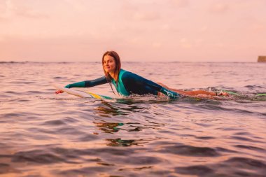 Okyanusta yüzen bir sörf tahtası üzerinde mükemmel bir vücut ile Surfgirl. Gün batımında sörf