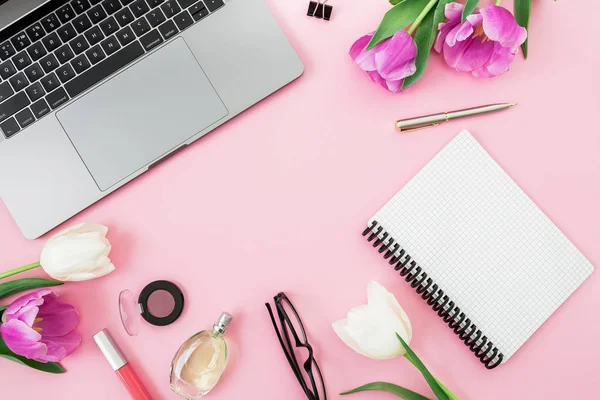Office composition with laptop, pink flowers, cosmetics, glasses and pen on pink background. Business concept. Flat lay. Top view.