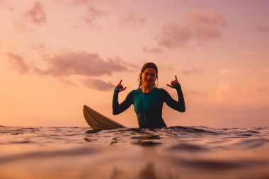 Gülümseyen sörfçü kadın okyanusta bir sörf tahtası üzerinde oturup. Gün batımında sörf