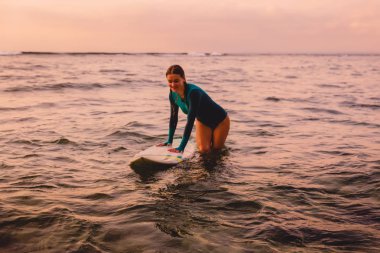 Okyanusta yüzen bir sörf tahtası üzerinde güzel surfgirl. Gün batımında sörf