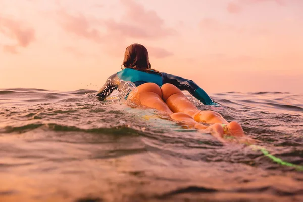 Okyanusta yüzen bir sörf tahtası üzerinde güzel surfgirl. Gün batımında sörf
