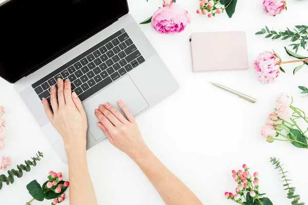 Woman typing on laptop. Workspace with female hands, laptop and pink flowers on white background. Top view. Flat lay. Copy space