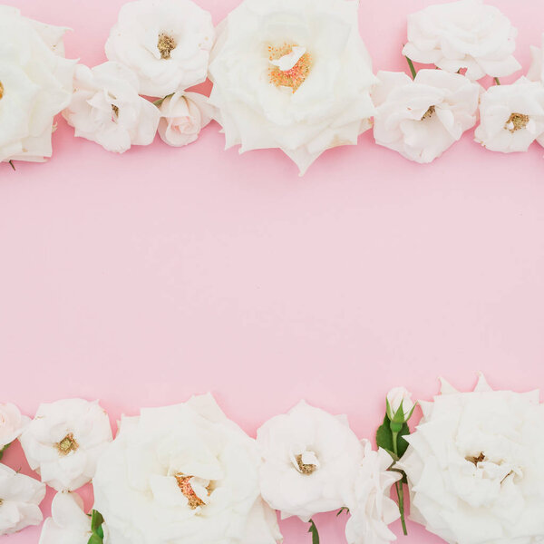 Frame with white roses on pastel pink background. Flat lay, top view.