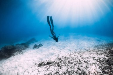 Genç kadın özgür dalgıç yüzgeçleri ile kumlu deniz üzerinde süzülüyor. Serbest dalış mavi okyanus
