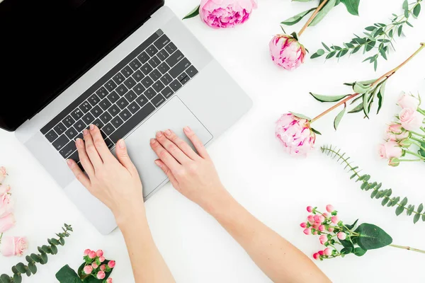 Woman blogger typing on laptop. Workspace with female hands, laptop and pink flowers on white background. Top view. Flat lay.