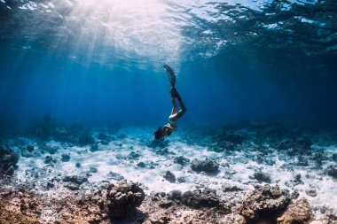 Genç kadın freediver mavi okyanusta yüzgeçleri ile kumlu deniz üzerinde süzülür.
