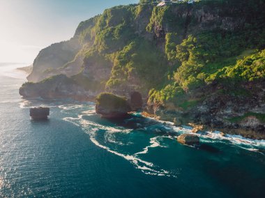 Rocky cliff and blue ocean with waves in Bali and beautiful light. Aerial view clipart