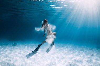 Kumlu deniz üzerinde yüzgeçleri ve beyaz kum ile kadın freediver. Mavi okyanusta su altında serbest dalış