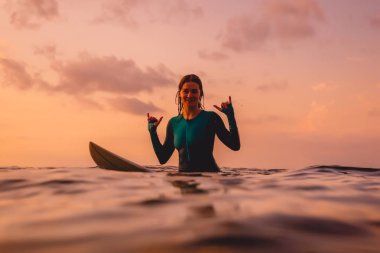 Okyanusta Sörf tahtası üzerinde gülümseyen sörf kız. Gün batımında sörf