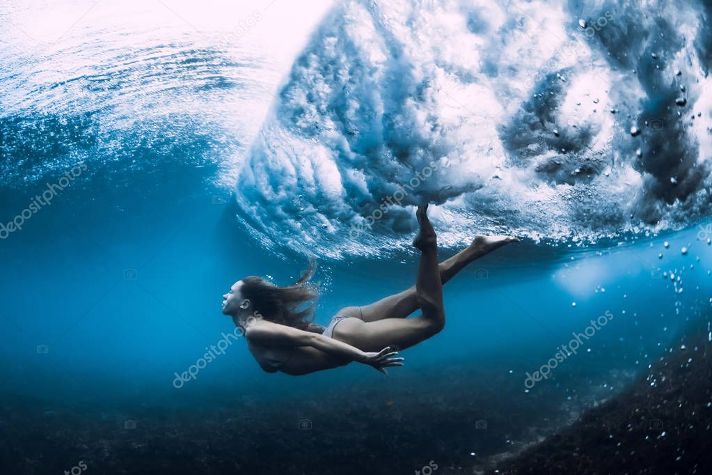 Woman swim underwater with ocean wave.