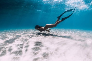 Çıplak kadın ücretsiz dalgıç yüzgeçleri ile kumlu deniz üzerinde süzülür. Freedivi