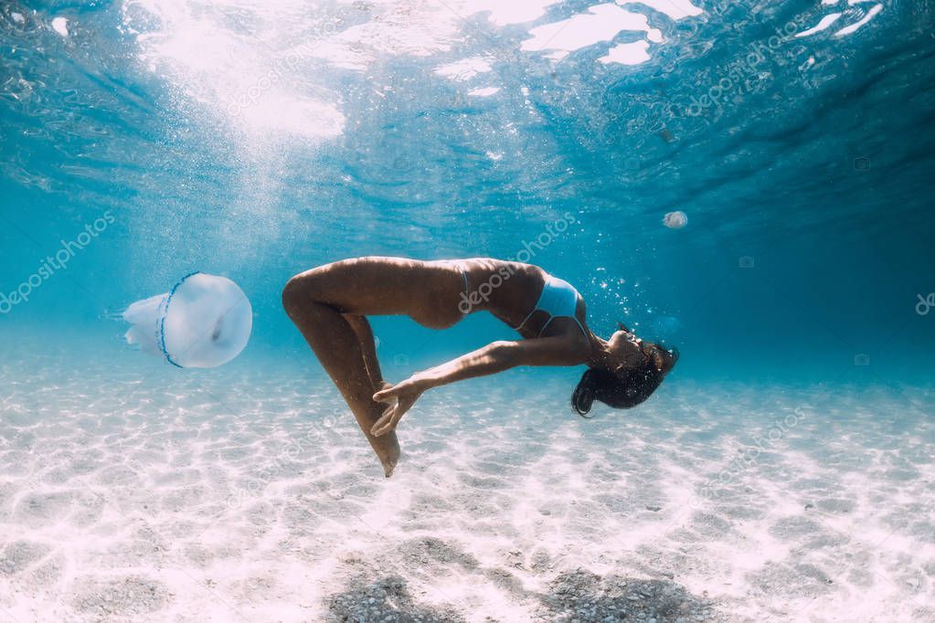 Woman diver glides over sandy sea with jellyfish. Freediving in 