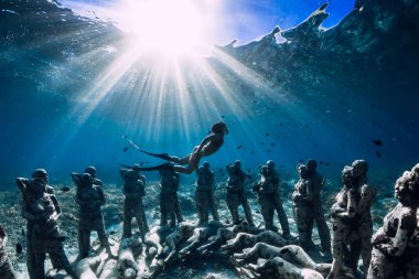 Yüzgeçli kadın serbest dalgıç sualtı heykellerinin yakınına daldı. Okyanusta sualtı turizmi.