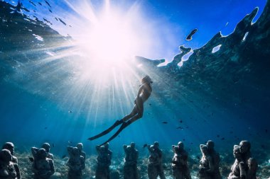 Yüzgeçli kadın serbest dalgıç sualtı heykellerinin yakınına daldı. Okyanusta sualtı turizmi.