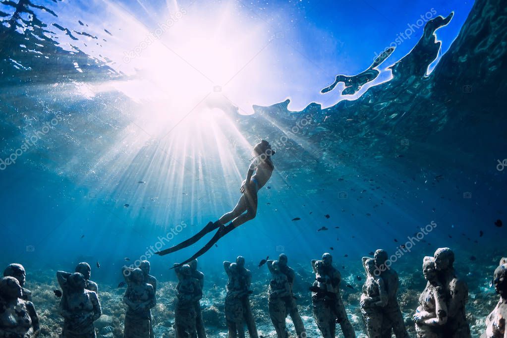 Woman freediver with fins dive near underwater statues. Underwater tourism in the ocean.