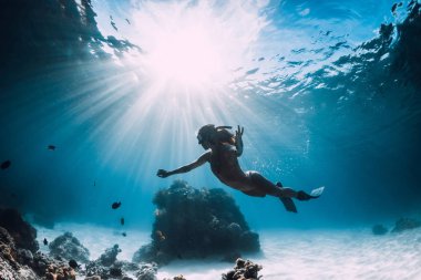 Yüzgeçli kadın freediver balık ve güneş ile kumlu deniz üzerinde yüzmek 