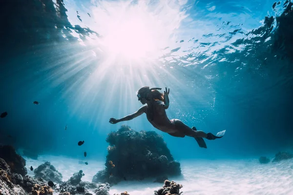 フィンを持つ女性フリーダイバーは、魚と太陽と砂の海の上を泳ぐ — ストック写真