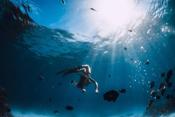 Девушка-фридайвер с плавниками ныряет с рыбами в голубом море — стоковое фото