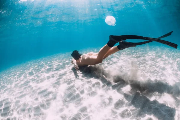 Freediver with fins glides over sandy sea in transparent ocean. Stock