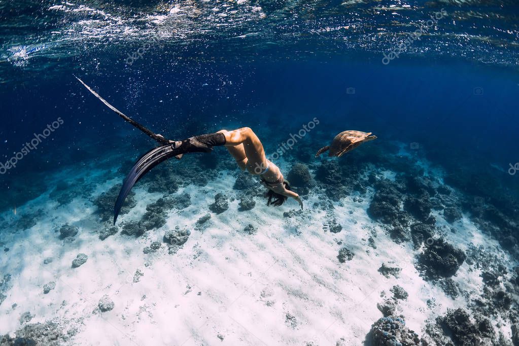 Woman freediver with fins glides underwater with sea turtle in t