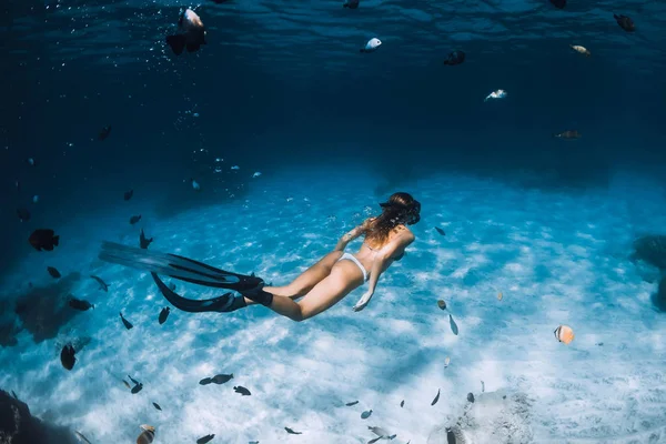 Freediver chica con aletas se desliza sobre fondo arenoso con peces en — Foto de Stock