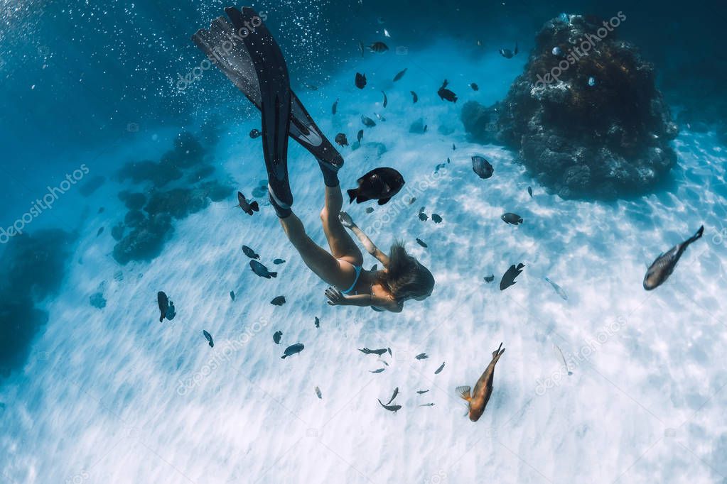 Freediver girl with fins glides over sandy bottom with fishes in