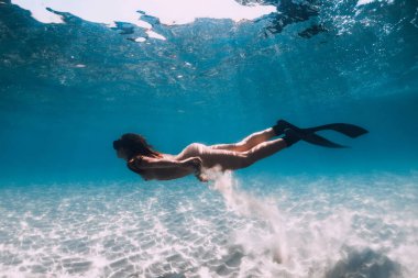 Yüzgeçli freediver şeffaf okyanusta kumlu denizin üzerinde süzülüyor.