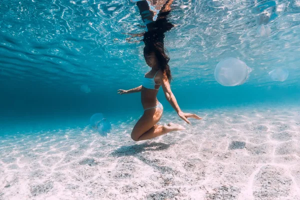 Mujer posando bajo el agua con medusas. Nadando en el océano azul — Foto de Stock