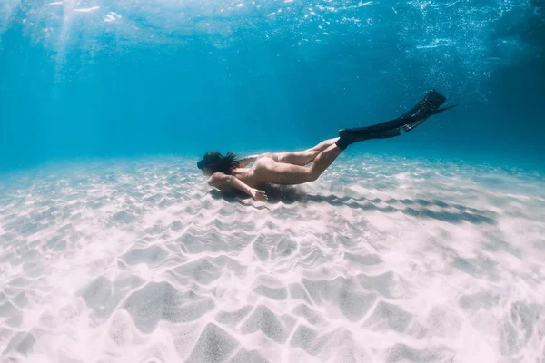 Freediver met vinnen glijdt over zandige zee in transparante oceaan. — Stockfoto