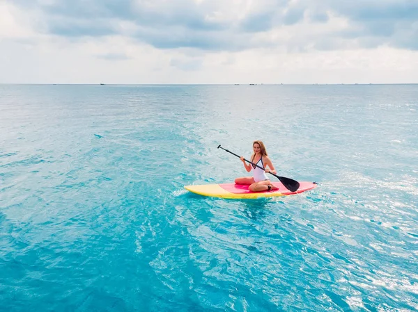 Belle femme debout planche à pagaie sur un océan bleu calme . — Photo