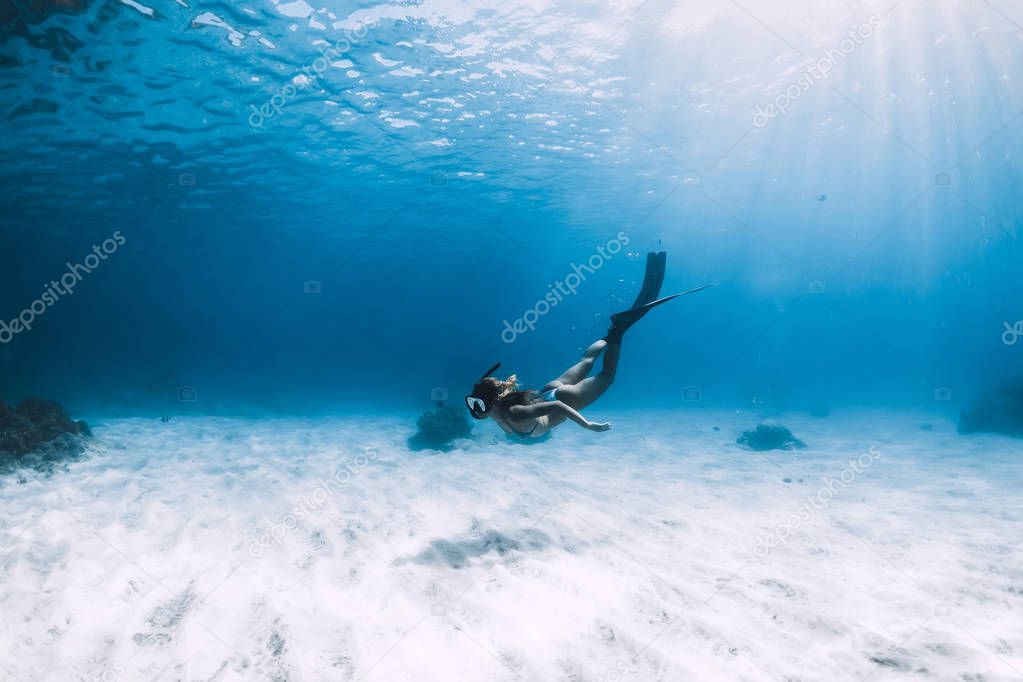 Attractive woman free diver glides with fins over sandy sea. Fre