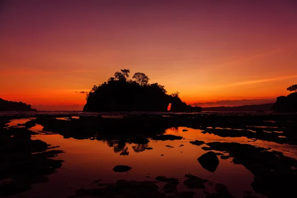 Isla de rocas en el océano con brillante puesta de sol caliente en Nusa Penida — Foto de Stock