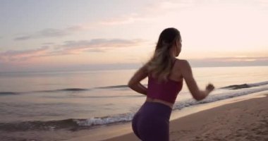 Gün batımı sahilinde koşan genç bir kadın. Deniz kıyısında koşan formda bir sporcu.