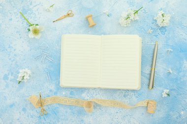 Beyaz günlüklü, püsküllü, makaslı ve mavi arka planda kalemli çiçeklerin yaz kompozisyonu. Düz yatış, üst görünüm