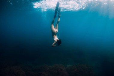 Yüzgeçleri suyun altına dalan bir kadın serbest dalgıç. Mavi okyanusta serbest dalış