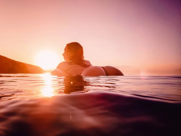 Young attractive woman floating in the sea at warm sunset. Sexy lady relaxing at summer ocean