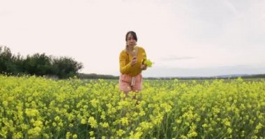 Sarı çiçeklerle dolu bir tarlada yürüyen mutlu bir kadın. Güzel kaygısız kadın çiçek açan tarlada doğanın tadını çıkarıyor.