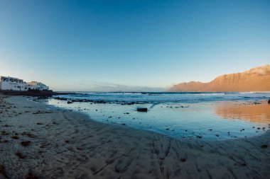 Lanzarote, Kanarya adalarında gün batımı tonları olan Famara plajı ve dağlar.