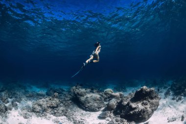 Kadın serbest dalgıç okyanusta suyun altında süzülüyor. Yüzgeçlerle serbest dalış