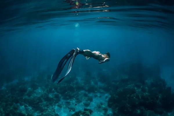 Woman free diver with fins swim underwater in transparent ocean