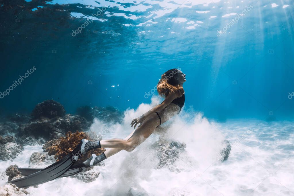 Woman freediver posing over sandy bottom with fins. Freediving in blue ocean at Hawaii islands