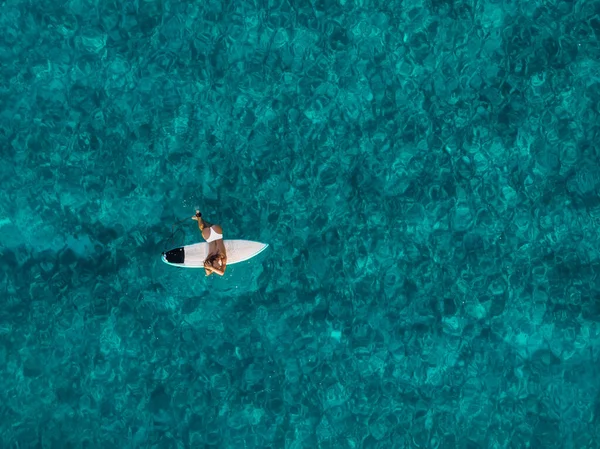 Attractive surfer woman on surfboard in blue ocean. Aerial view