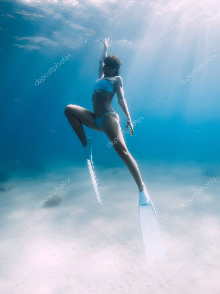 Freediver glides over sandy sea with white fins. Attractive woman free diver in blue ocean