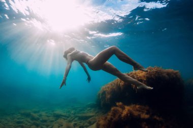 Suyun altında poz veren bir model. Çıplak kız yaz denizinde güneş ışığıyla süzülüyor.