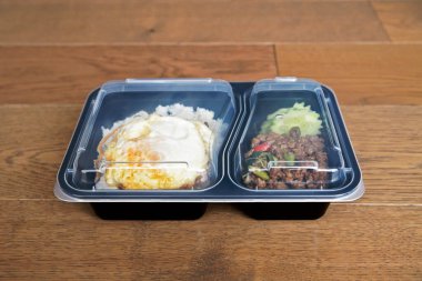Fesleğen pilavı, ahşap zemine temiz kapaklı siyah plastik bir kutuya konur. Bu yemek Tayland 'da popüler bir sokak yiyeceğidir..