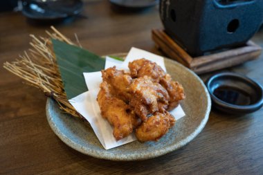 Japon usulü garnitürlü kızarmış tavuk, bir fincan sos ve bir Japon izakaya restoranında koyu kahverengi ahşap bir masada soba..